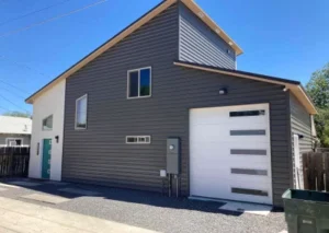 A modern two-story house with a gray exterior, large garage door, and a bright blue front door, set against a clear blue sky