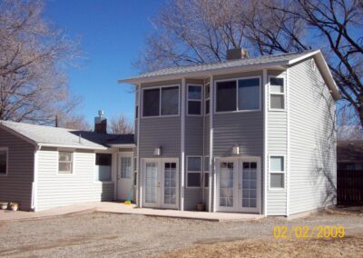 A two-story grey siding home addition featuring two sets of white double glass doors and multiple sliding windows